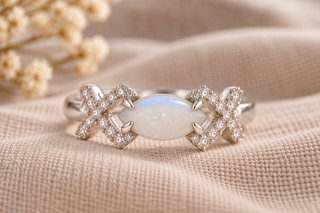 Sterling silver Elara breastmilk inclusion ring with a marquise-shaped breastmilk stone in blue hue and sparkling cubic zirconia crossover detailing, photographed on soft neutral linen.
