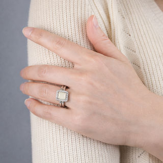 Hand wearing a silver ring with a pure breastmilk stone against a neutral background