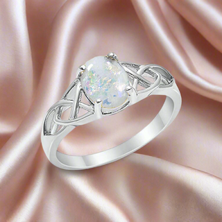 Sterling silver Celtic knot ring with oval breast milk inclusion stone with opal flakes on a soft satin background.